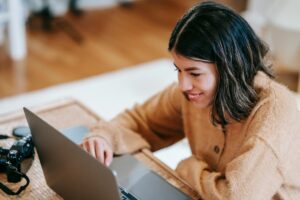 Smiling remote employee experiencing the benefits of flexible work culture while collaborating on her laptop from a cozy, personalized home office - VirtualPro Solutions