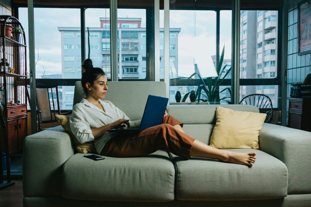A woman in her laptop working cozily in her home at her living room - VirtualPro Solutions