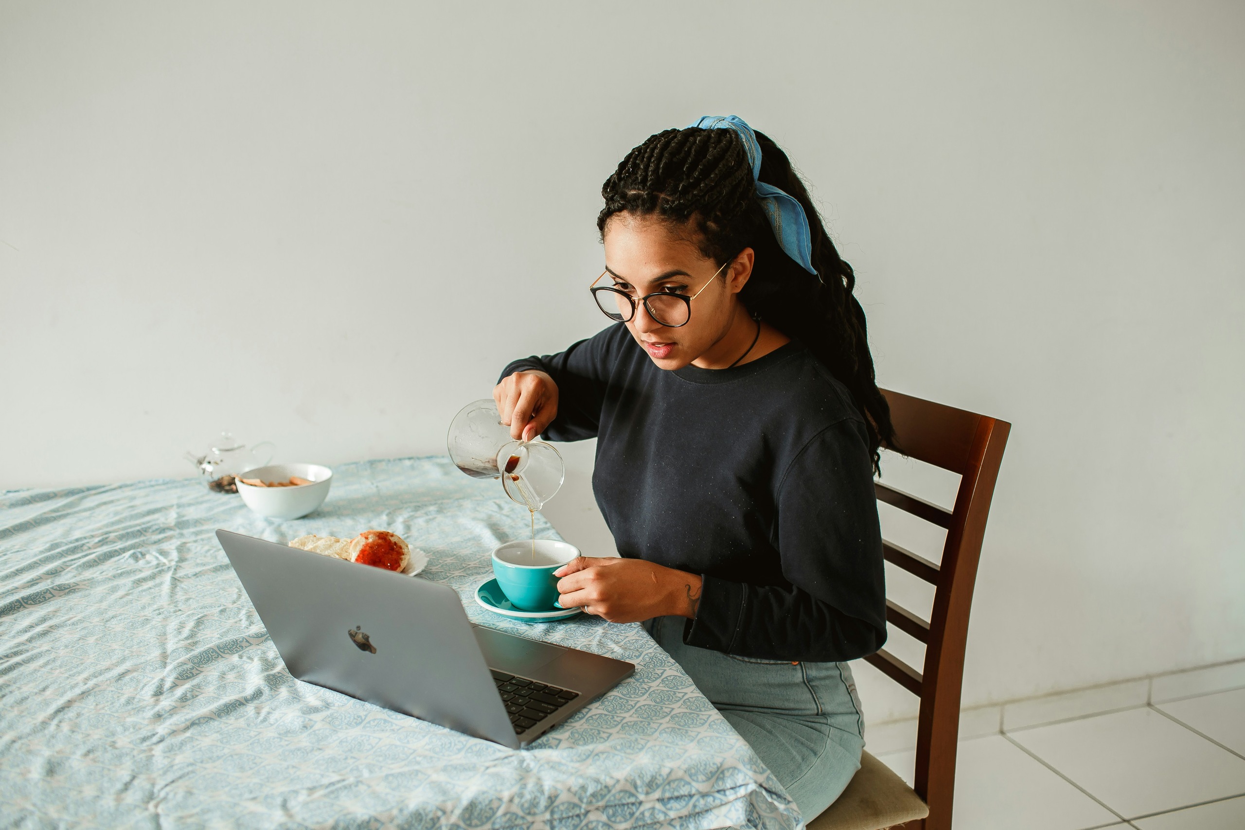 A remote professional taking her morning coffee break while staying productive at her laptop in a bright, clean home workspace.